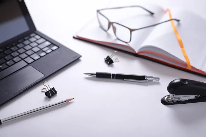 Un ordenador portátil negro, un cuaderno abierto con gafas