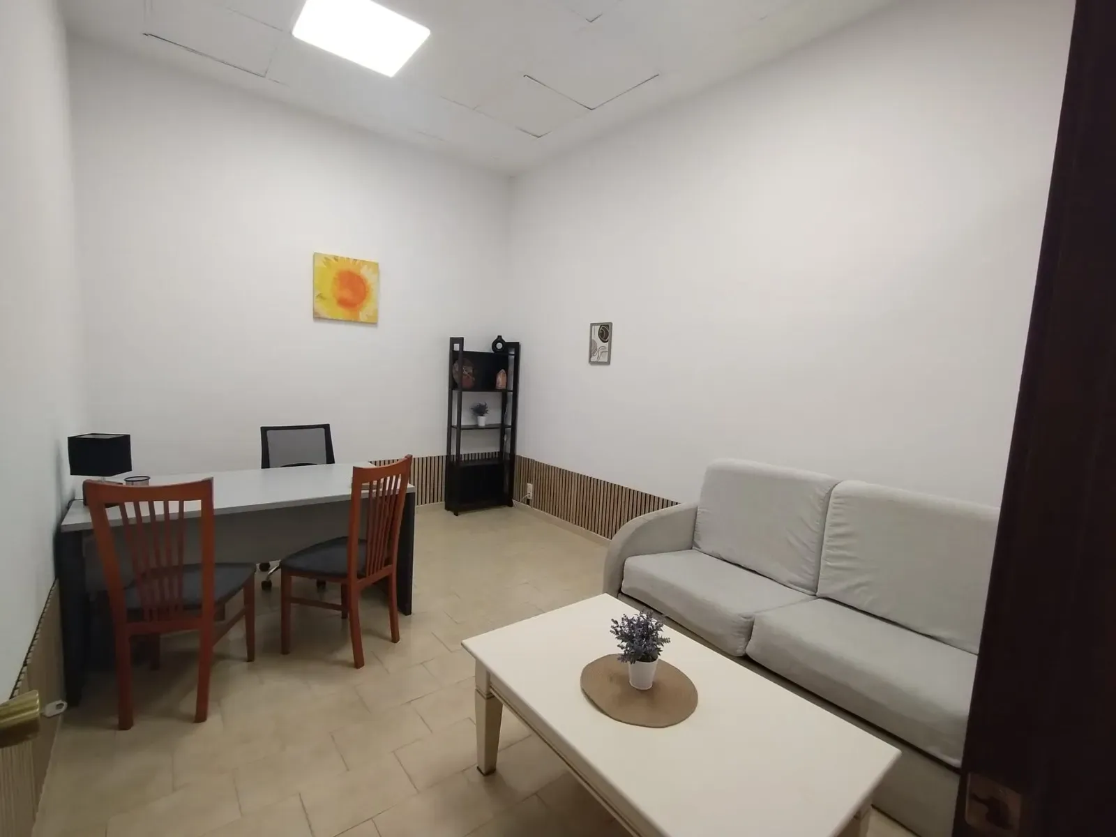 Una oficina sencilla con un escritorio con dos sillas de madera, un sofá claro