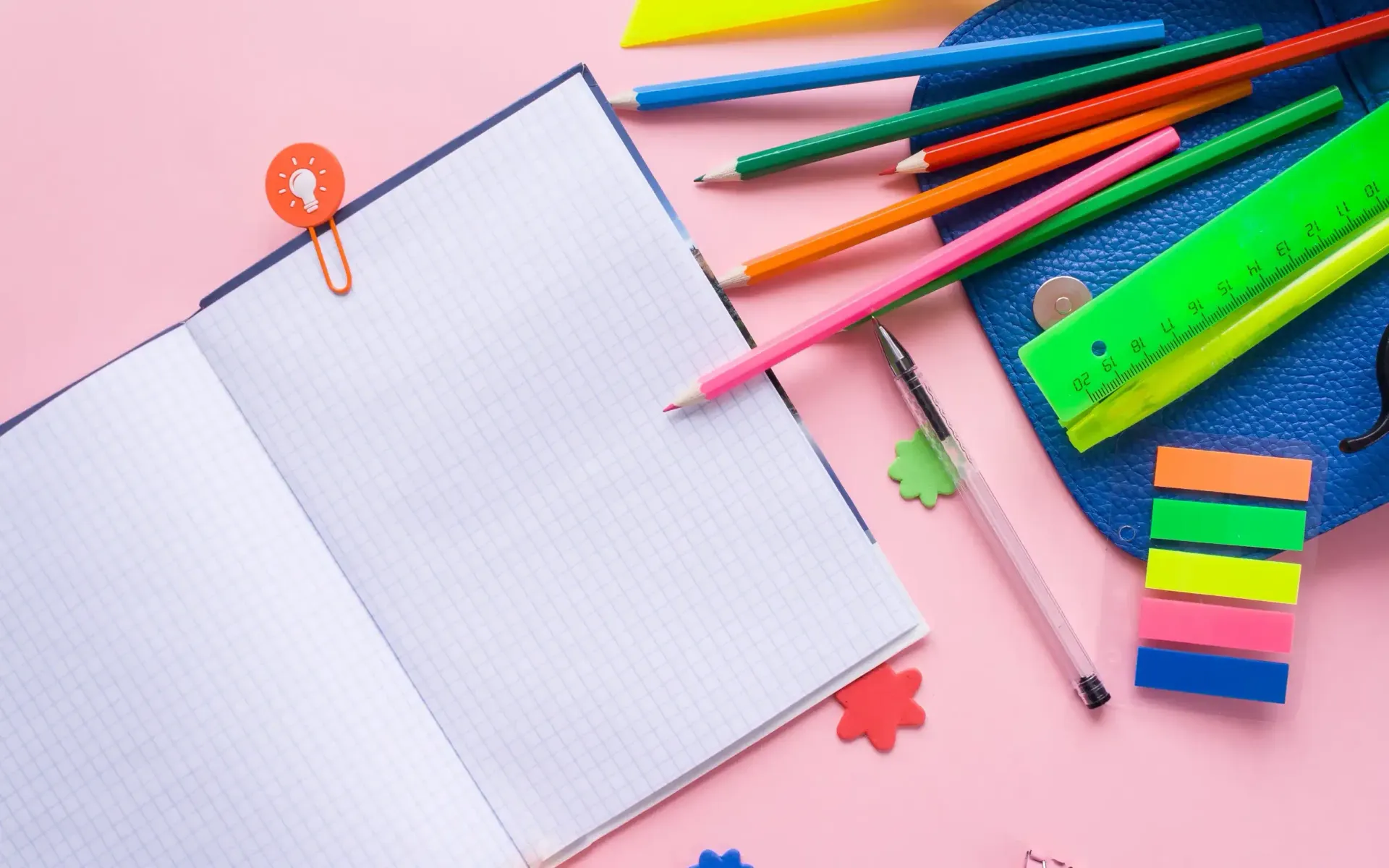 Un cuaderno abierto con un clip en forma de bombilla, lápices de colores