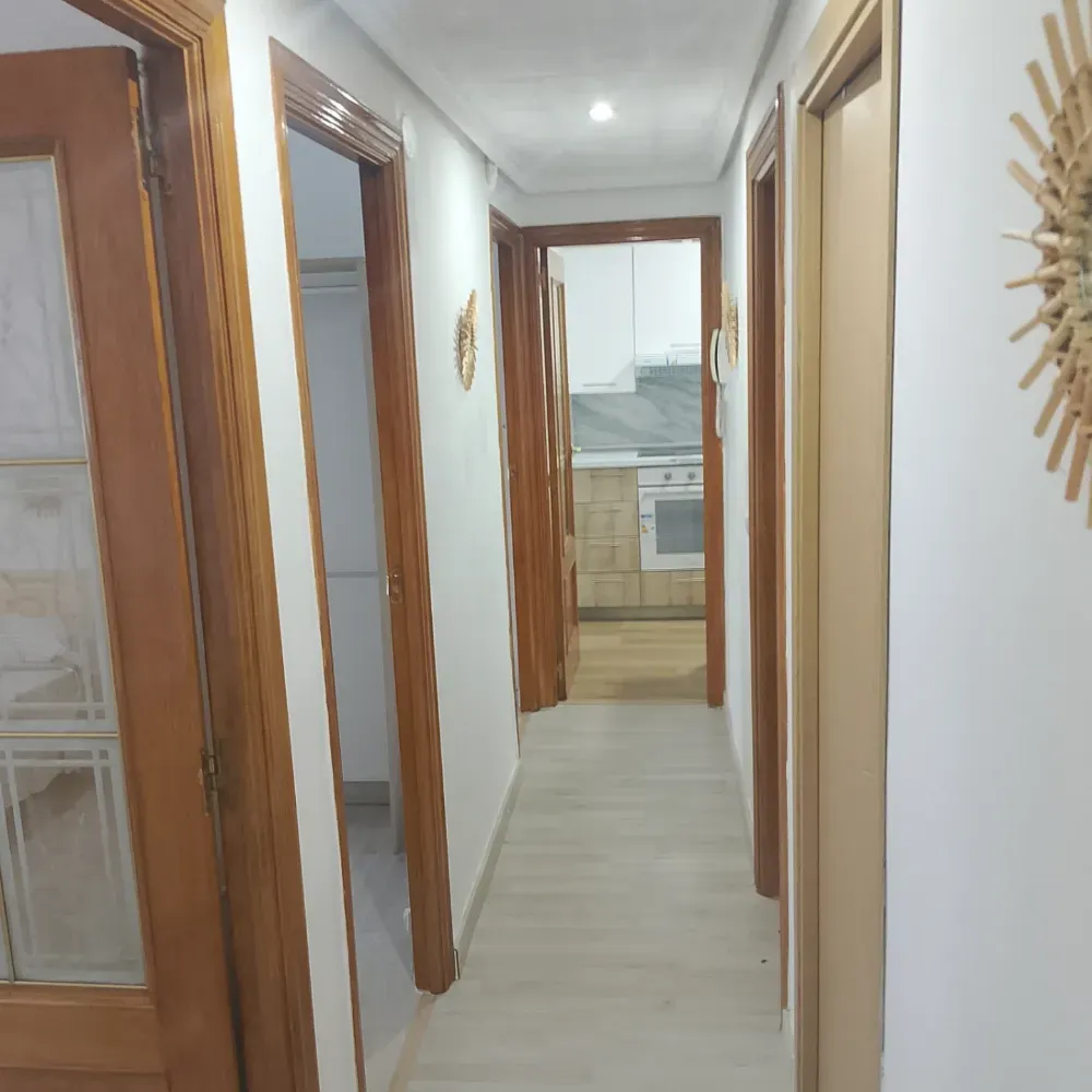 Pasillo estrecho con puertas revestidas de madera que conduce a una cocina luminosa.