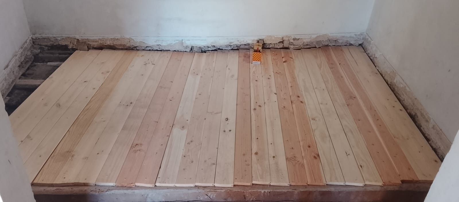 Suelo de madera recién instalado en una pequeña habitación sin terminar, con paredes blancas y bordes a la vista