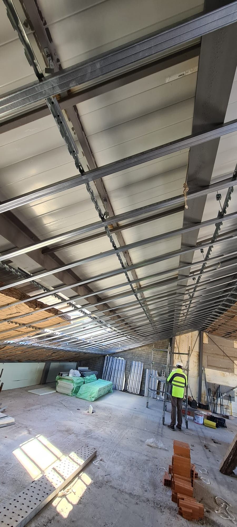 Interior de un edificio en construcción, con vigas de acero a la vista, trabajadores y materiales dispersos por el suelo