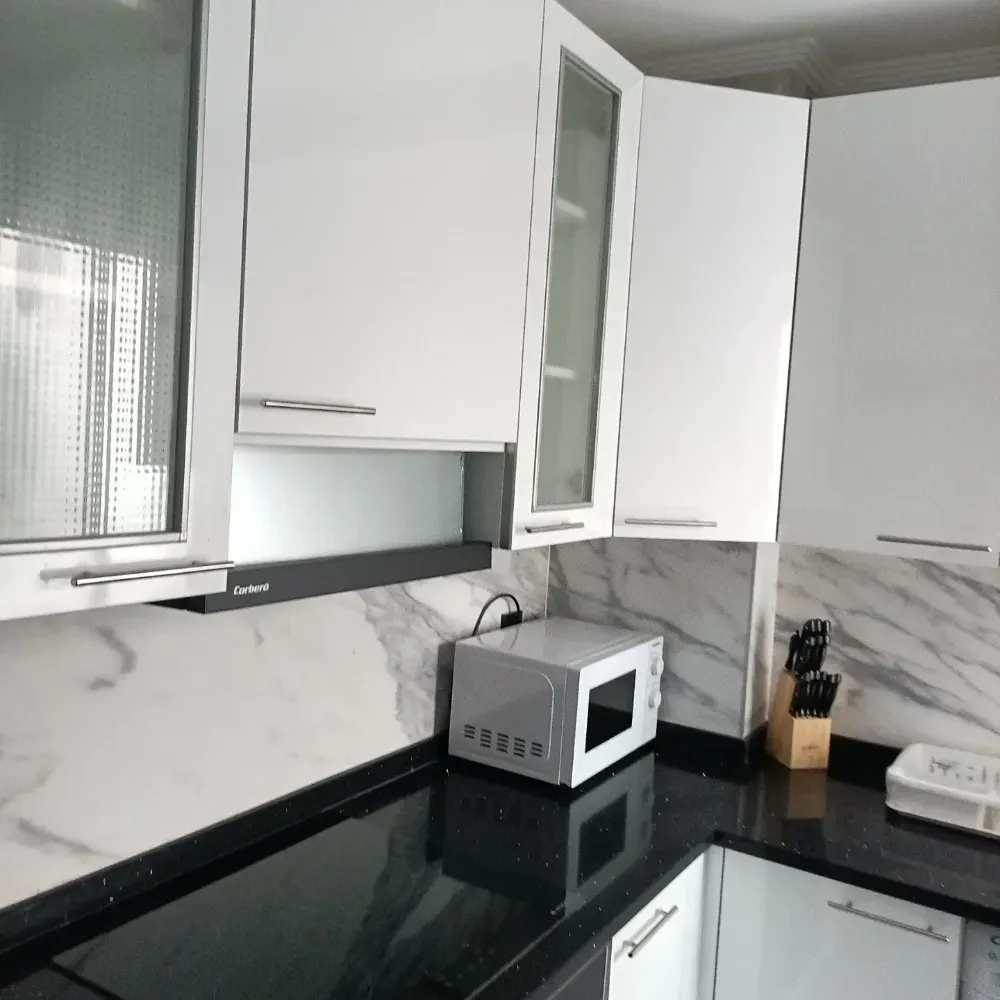 Cocina moderna con gabinetes blancos, salpicadero de mármol, encimera negra, microondas y bloque para cuchillos.