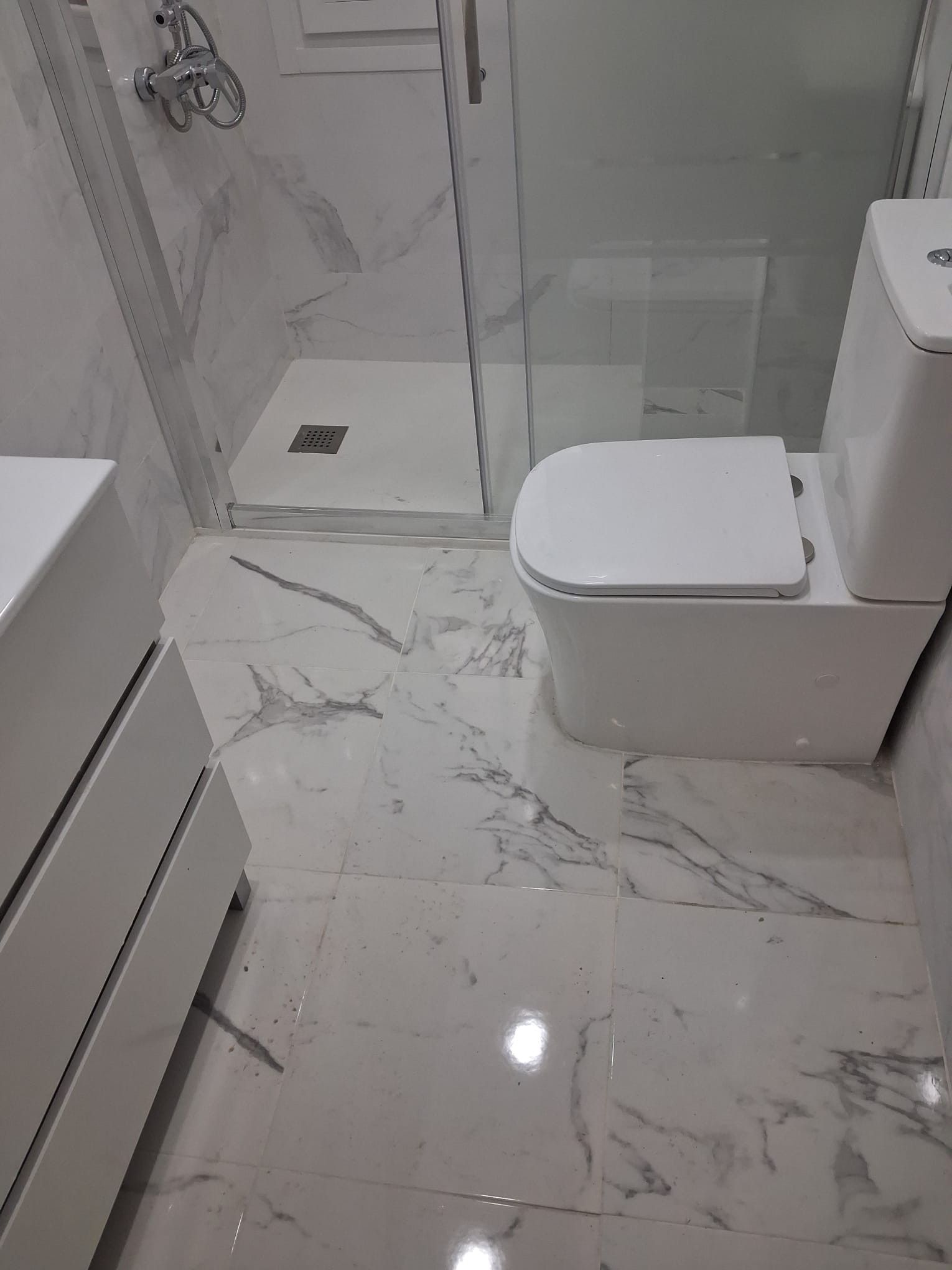 Baño moderno blanco con azulejos de mármol, ducha a ras de suelo e inodoro a la derecha