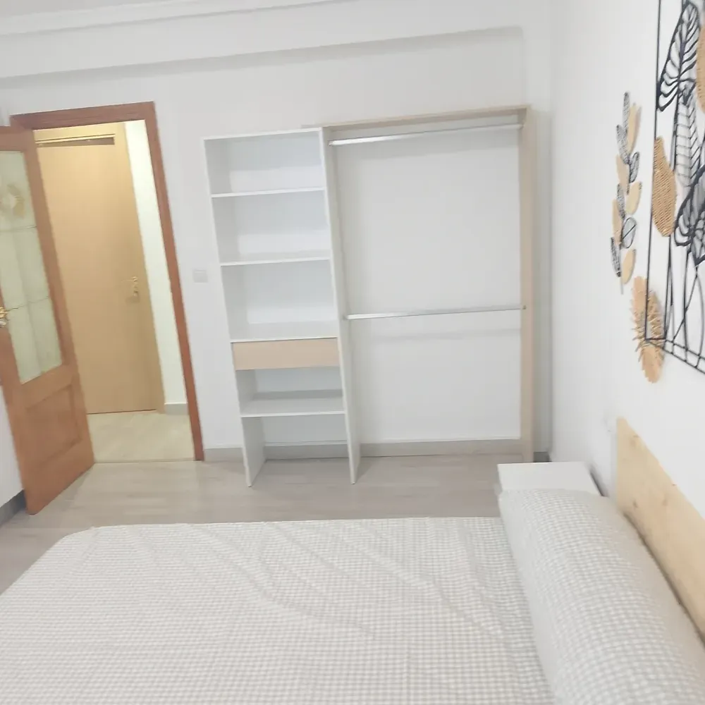 Habitación luminosa con puerta abierta, estanterías blancas y cama con edredón ligero.