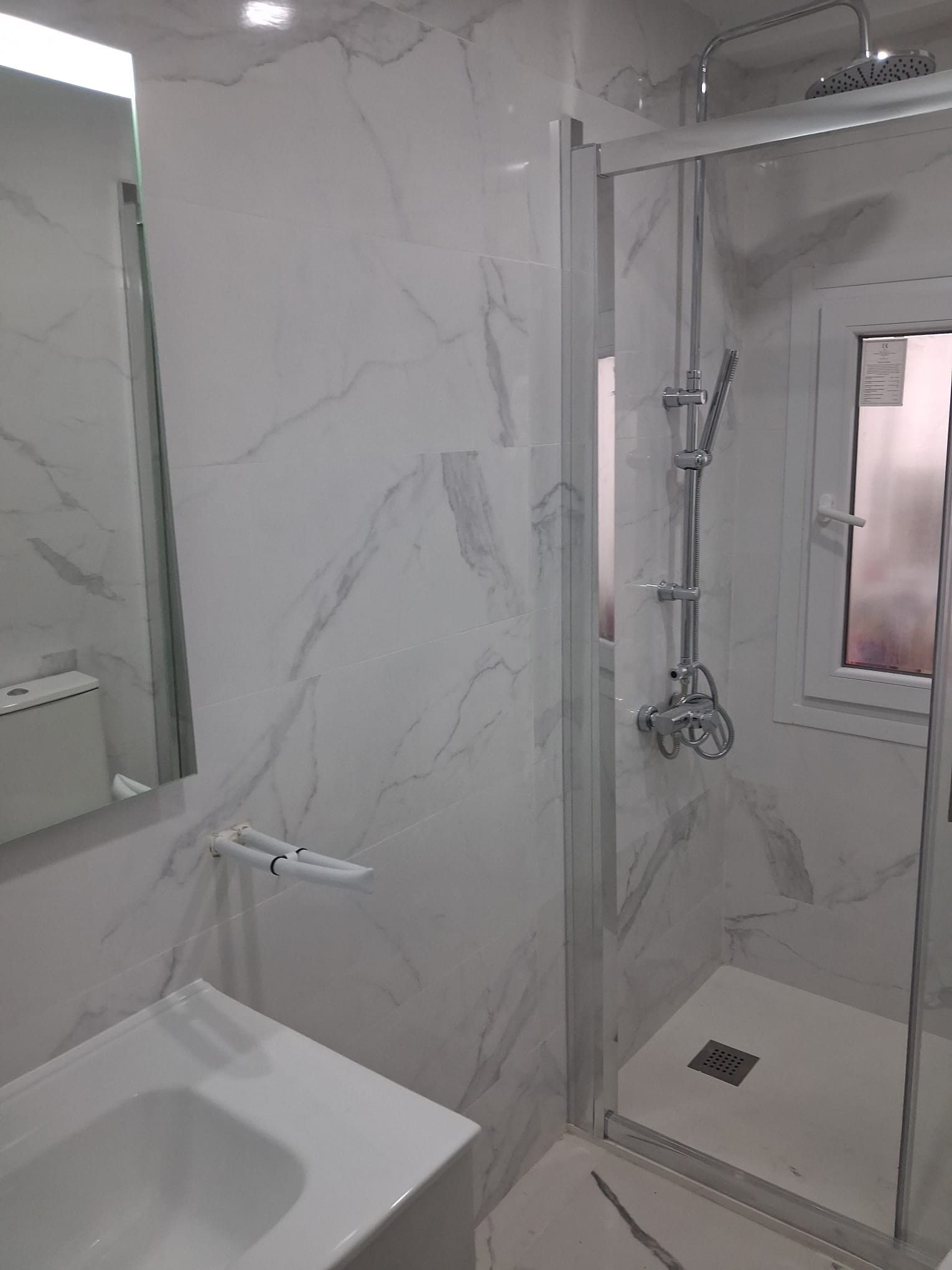Baño moderno con azulejos efecto mármol, espejo de pared, lavabo y mampara de ducha de cristal