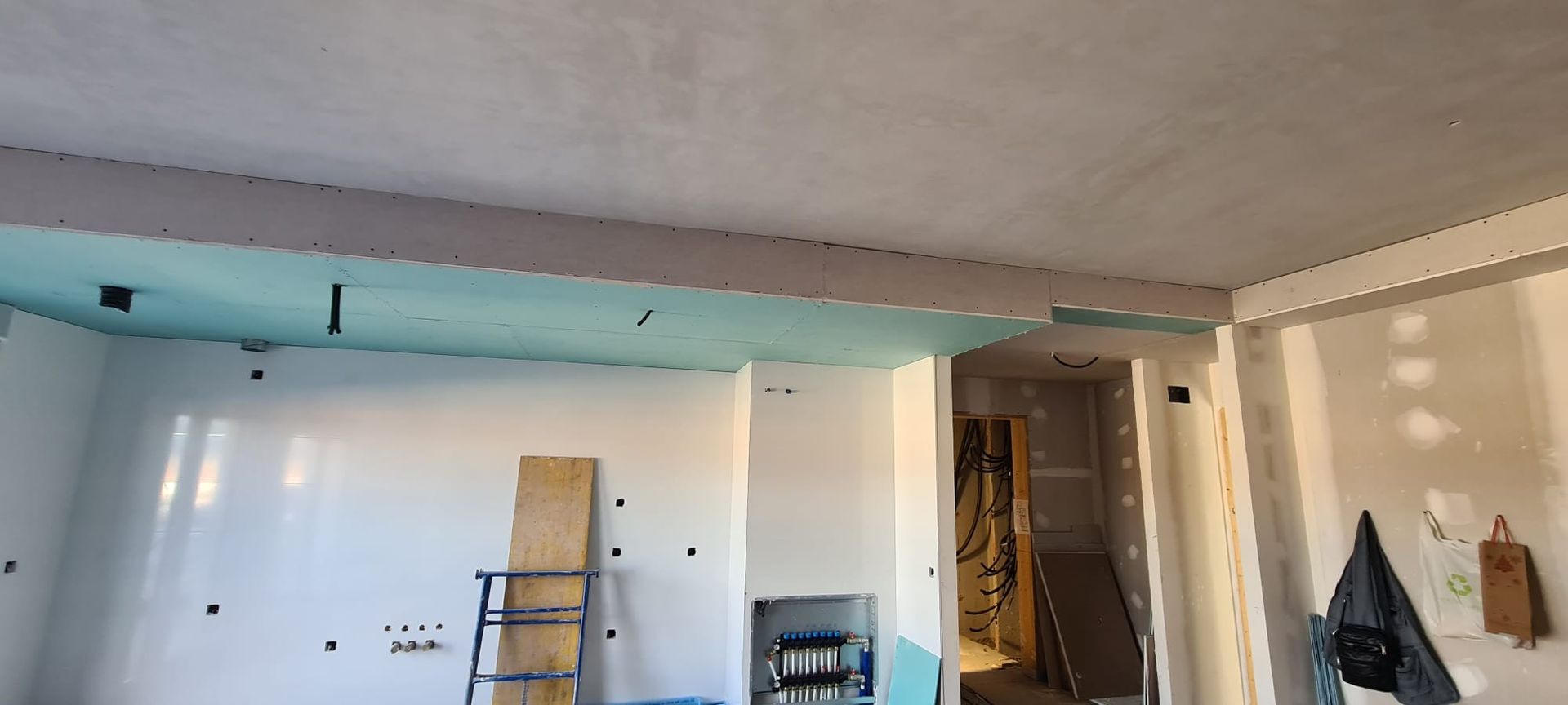 Habitación sin terminar del todo, con paneles de yeso, luces turquesas en el techo, una escalera y materiales de trabajo