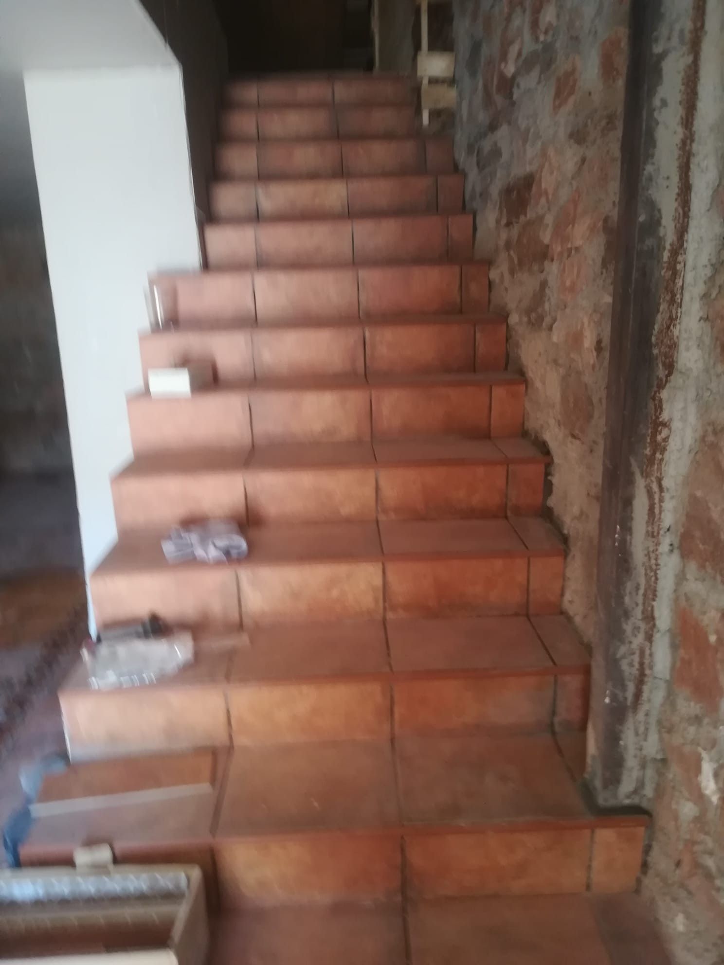 Escalera interior de baldosas con peldaños de terracota y una pared rugosa sin terminar a la derecha