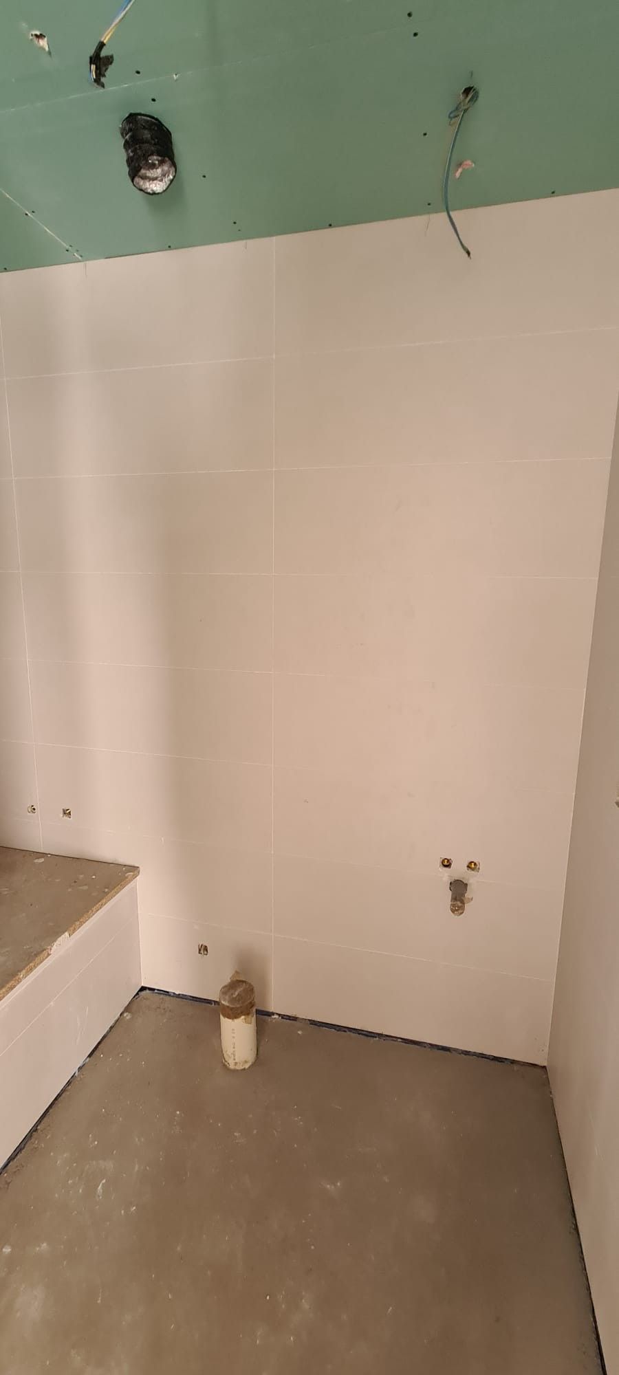 Pared de baño desnuda con instalaciones de fontanería y pintura sin terminar sobre una abertura en el suelo