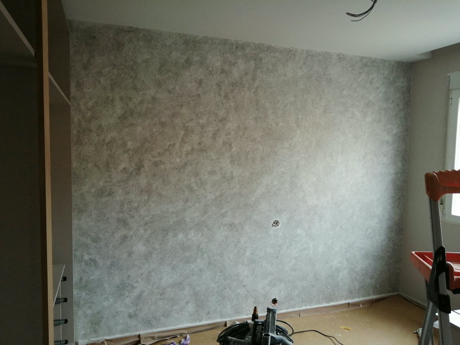 Habitación vacía con papel pintado gris texturizado, una ventana a la derecha y un armario a la izquierda.
