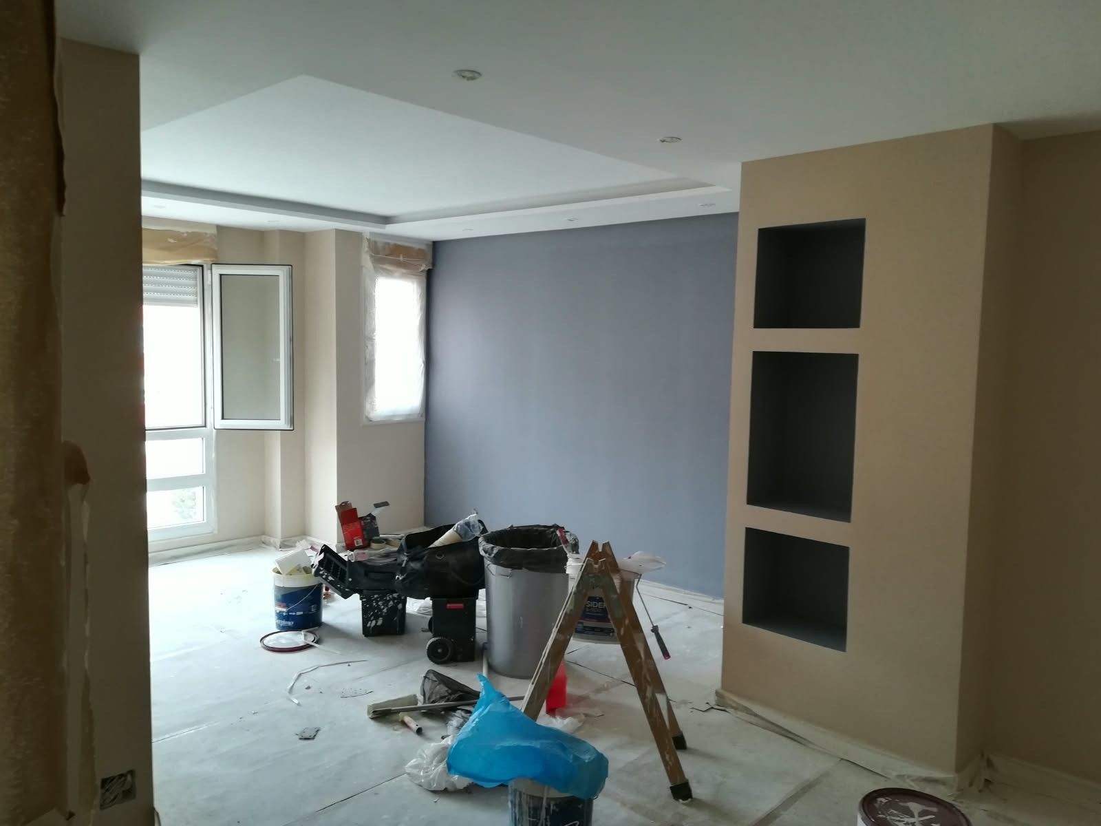 Habitación renovada con material de pintura, una escalera y una pared de acento gris junto a una ventana