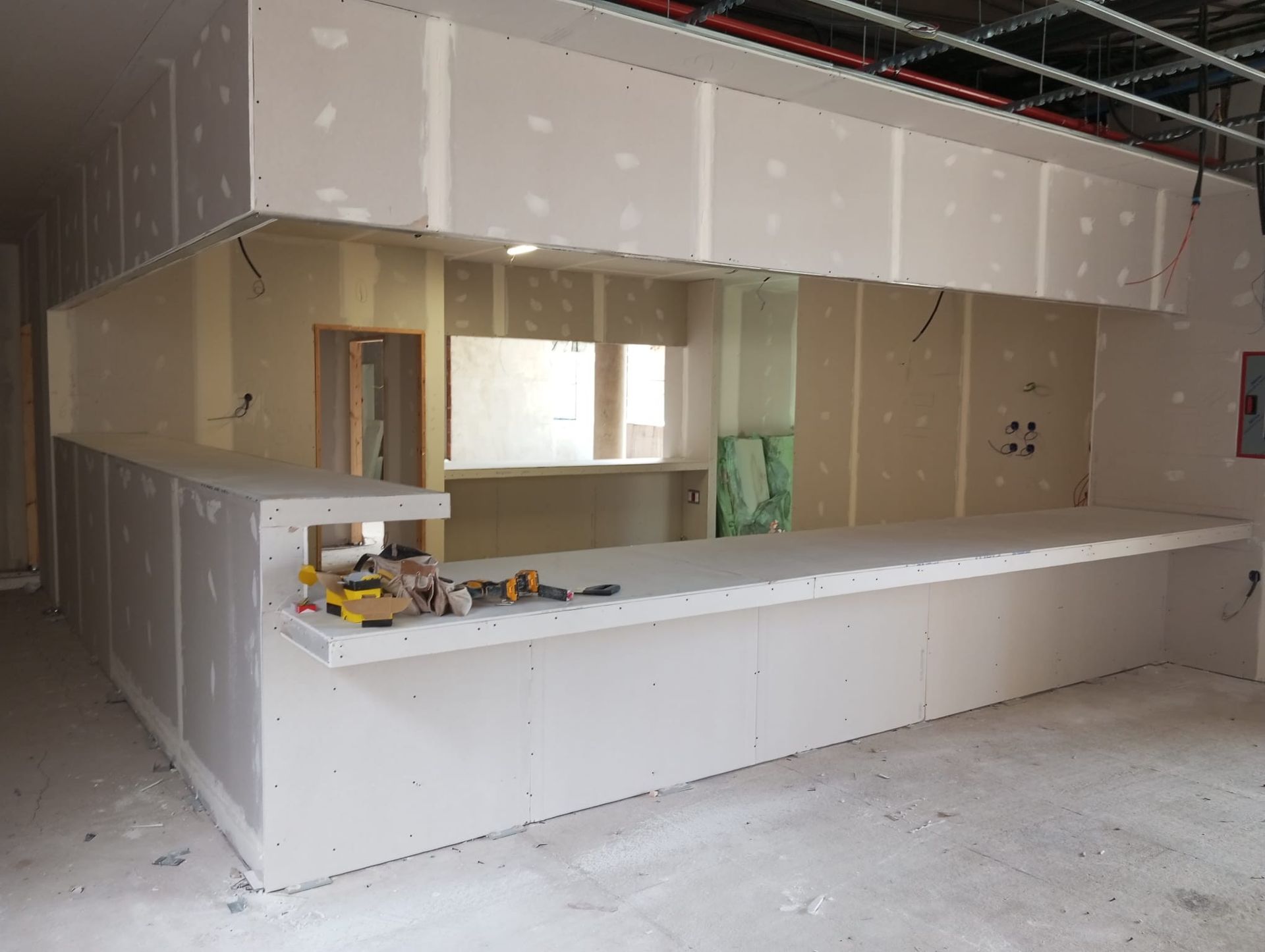Cocina parcialmente terminada, con península blanca, armarios beige y paredes de yeso en construcción