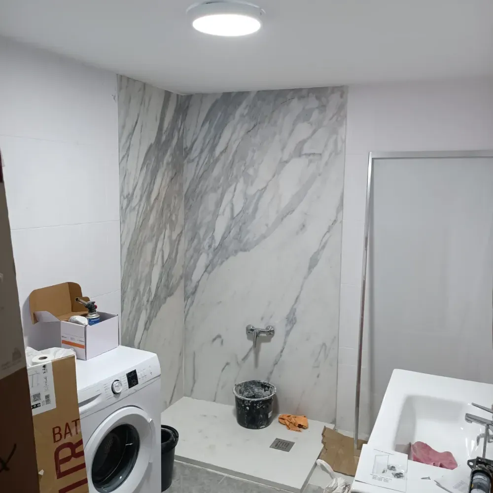 Cuarto de lavandería con lavadora y panel de pared con diseño de mármol en proceso de renovación.