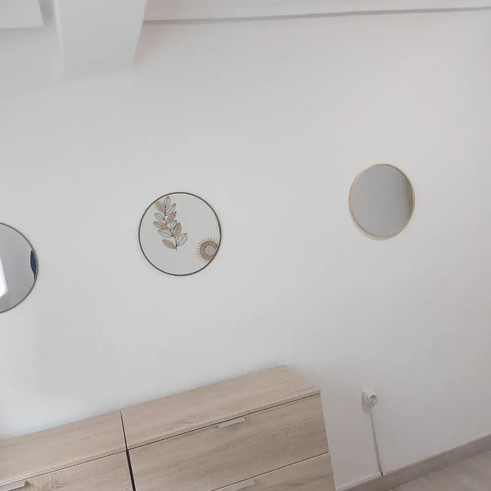 Habitación blanca con tres espejos redondos sobre un mueble de madera clara, interior minimalista.