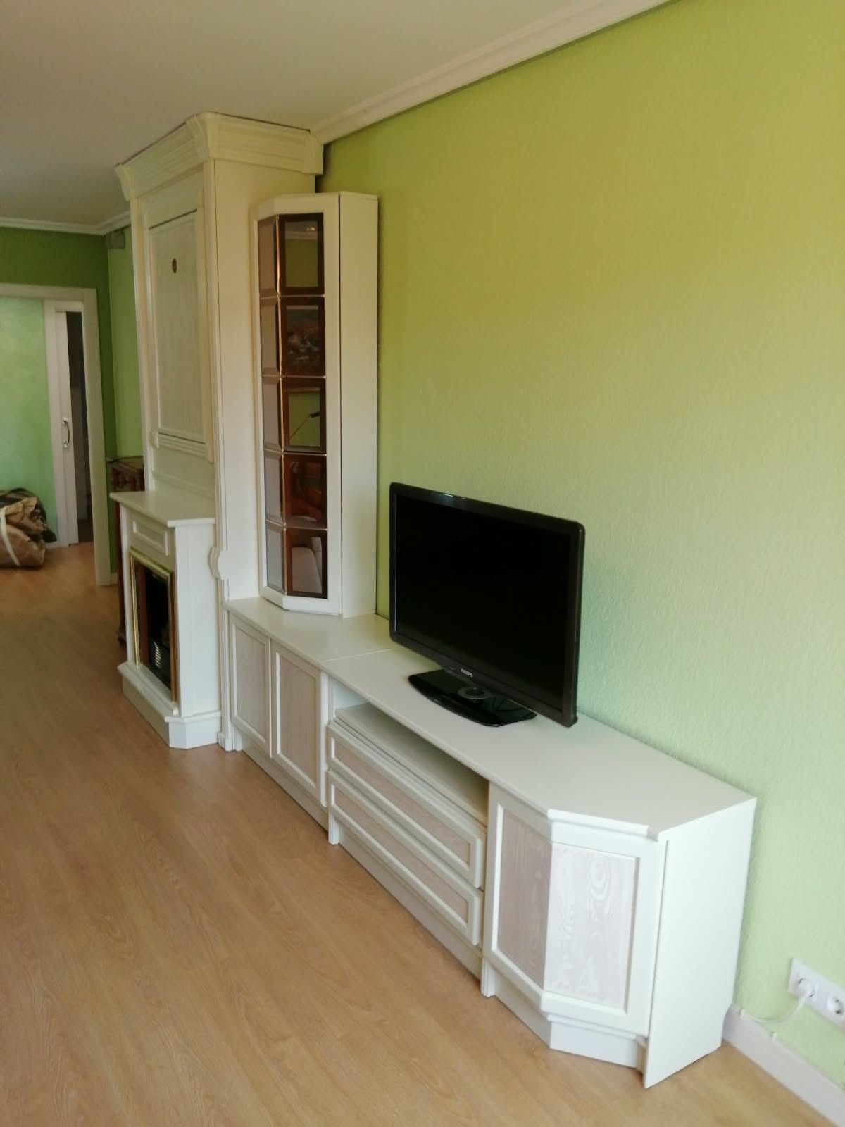 Salón luminoso con paredes verde lima, mueble blanco para la televisión, televisor de pantalla plana y estantería alta.