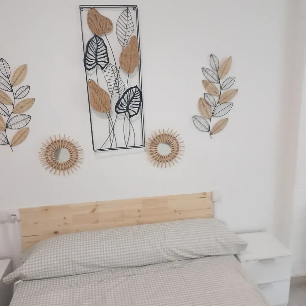 Dormitorio minimalista con cama de madera, ropa de cama gris y decoración de pared con hojas en tonos neutros sobre el cabecero.