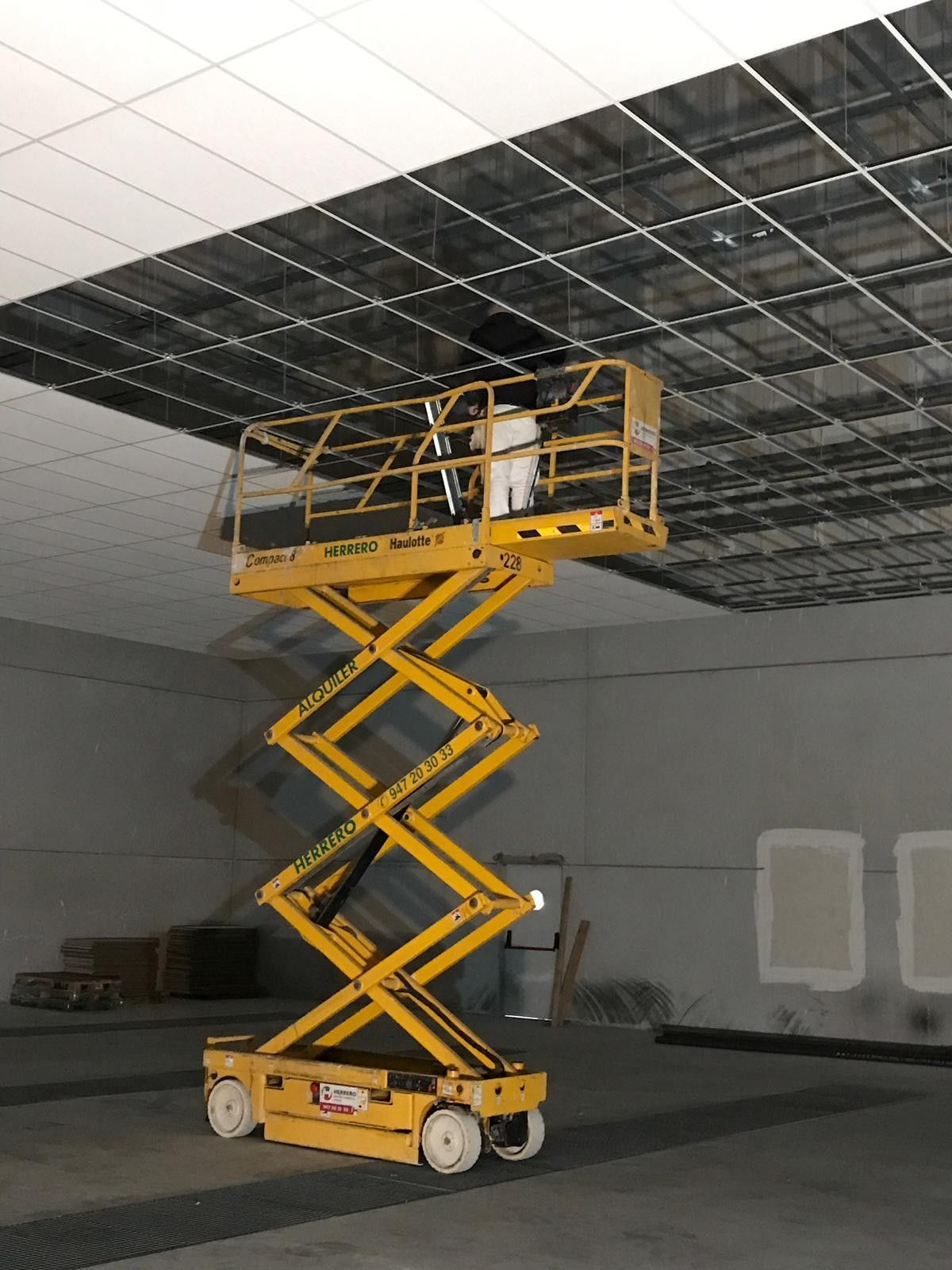 Una plataforma elevadora de tijera amarilla elevada hasta el techo en una habitación oscura sin terminar