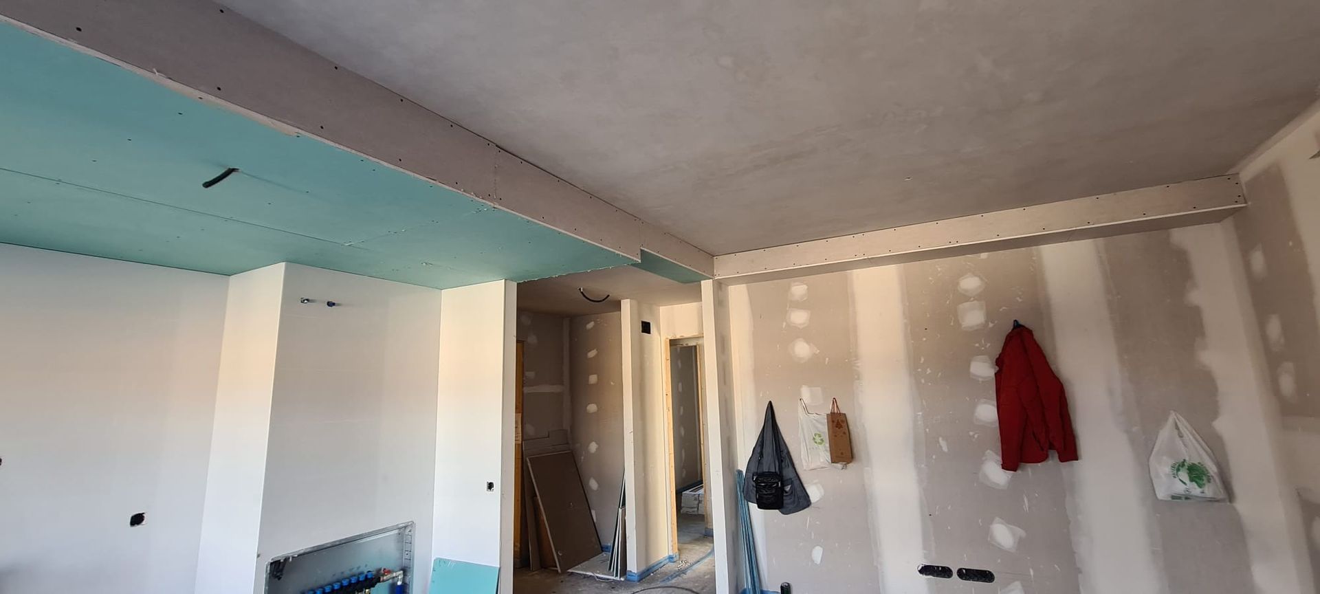 Habitación vacía con papel pintado a rayas, una viga azul en el techo y abrigos colgados en la pared.