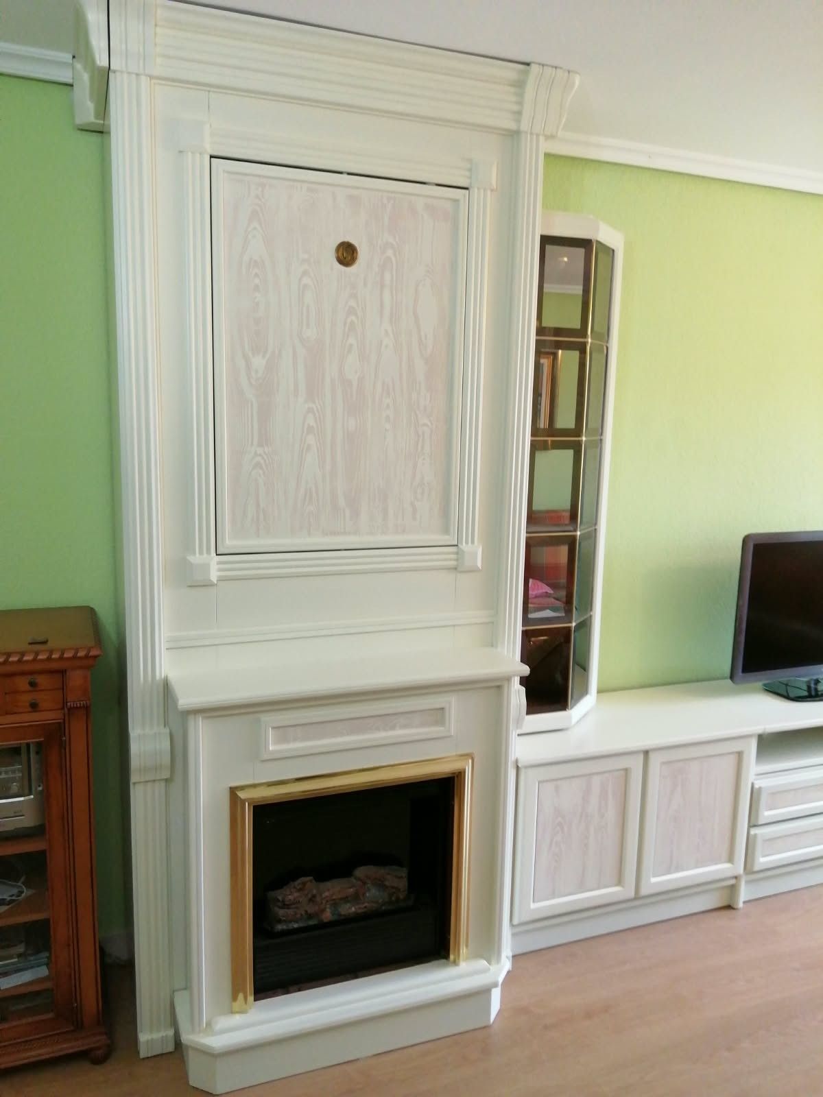 Mueble empotrado blanco con chimenea y módulo multimedia en un salón verde claro, con un televisor a la derecha.