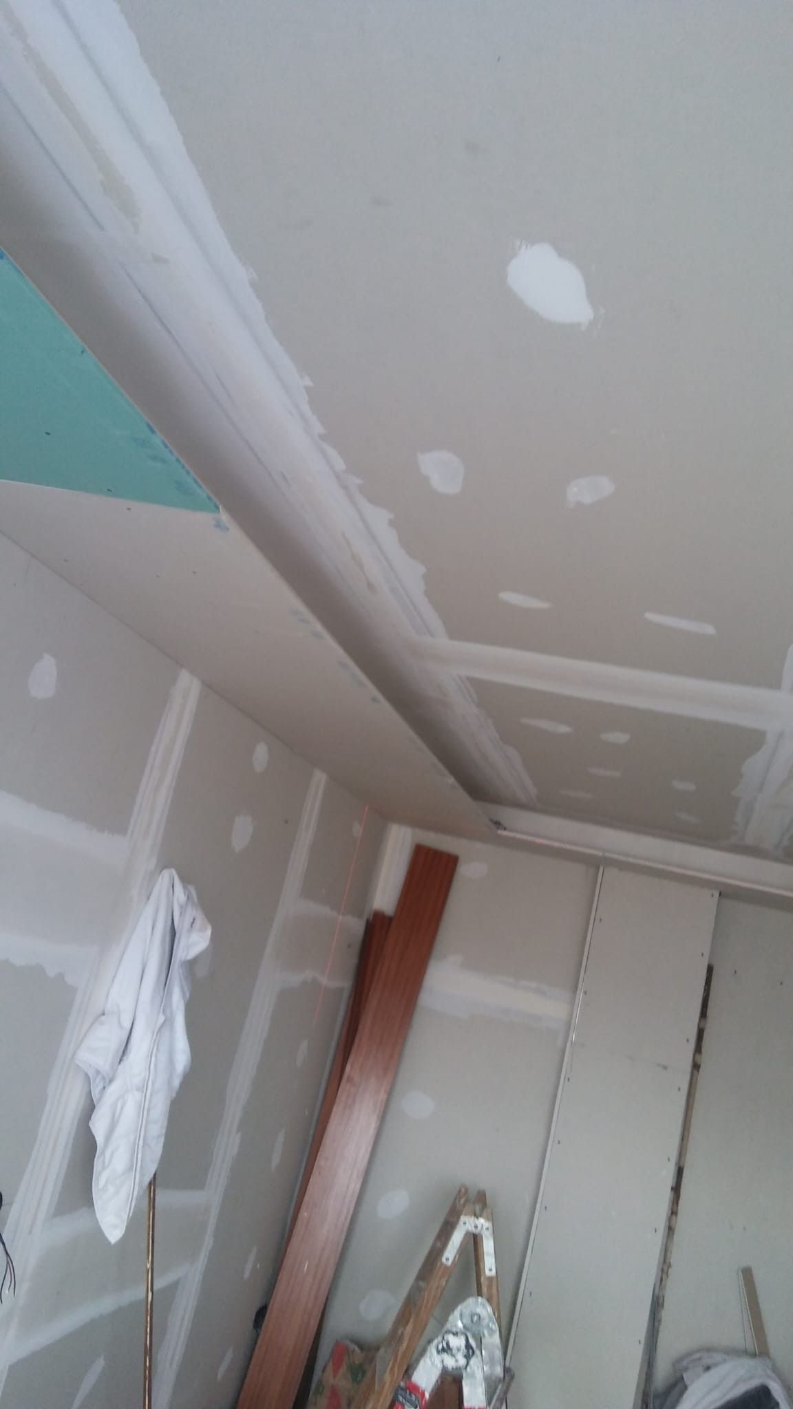 Renovación de una habitación con parches de paneles de yeso en el techo y las paredes, y una escalera de tijera debajo.