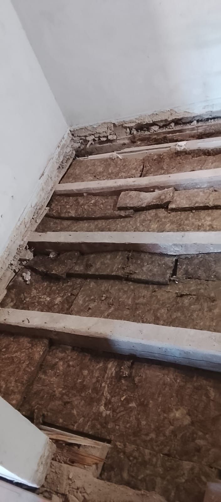 Escalera estrecha con peldaños de madera rotos y cubiertos de polvo en un interior de paredes blancas