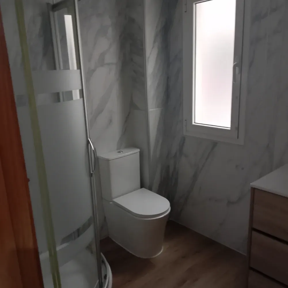 Baño moderno con ducha de cristal, inodoro suspendido, lavabo de madera y paredes con diseño de mármol.