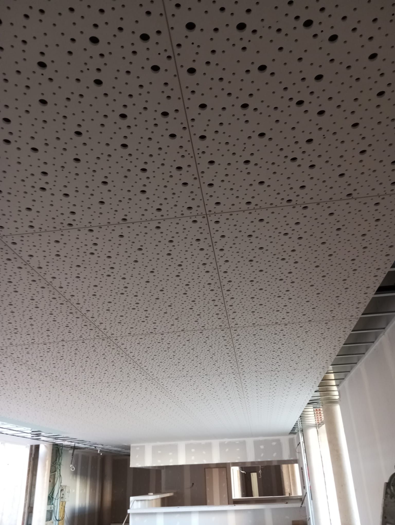 Techo con paneles acústicos perforados en una sala moderna con ventanas y cortinas