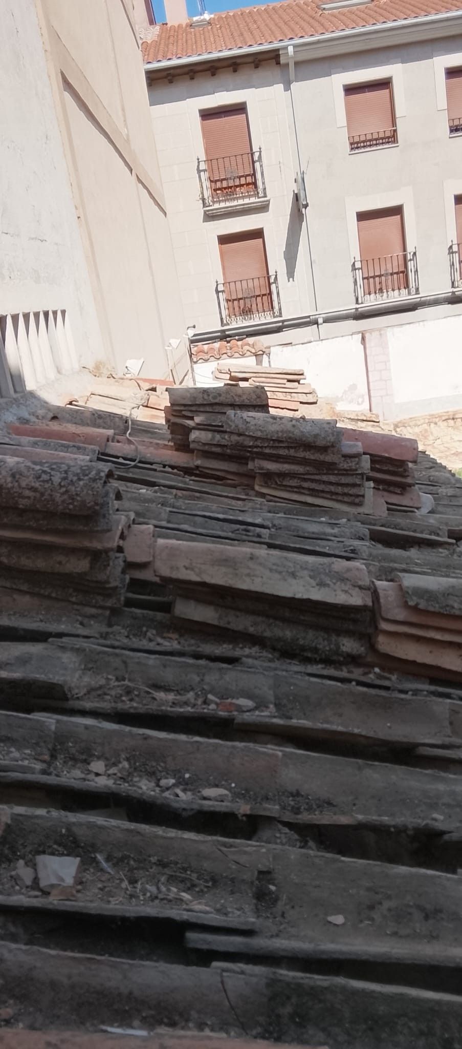 Escalones de piedra que conducen a un patio soleado, rodeado de edificios claros con tejados de tejas rojas.