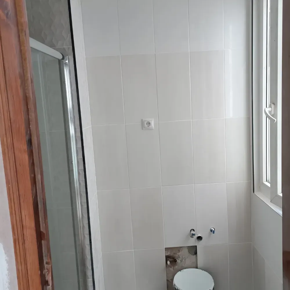 Pared de baño vacía con azulejos, ventana y toma de agua en construcción.