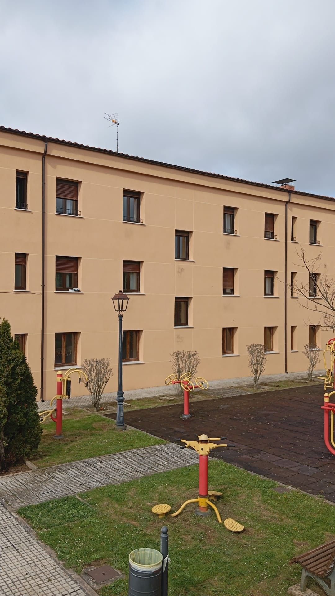 Edificio de apartamentos junto a una pequeña zona de ejercicio al aire libre con equipos de entrenamiento de colores en un día nublado