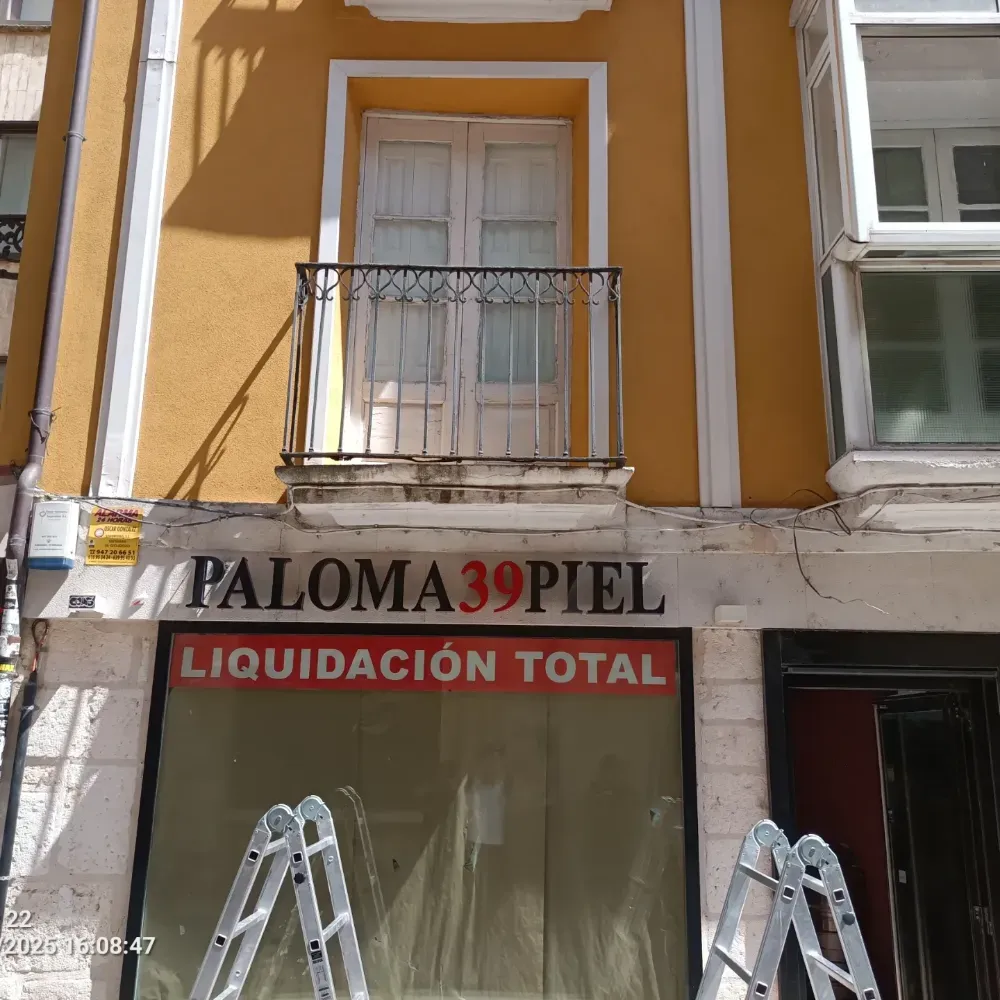 Fachada de local comercial con letrero “PALOMA39PIEL” y pancarta roja “LIQUIDACIÓN TOTAL”, con dos escaleras de mano en el exterior.