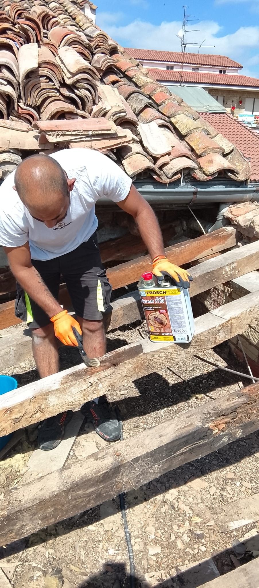 Un trabajador reparando un tejado de tejas con herramientas sobre tablones de madera bajo un sol radiante