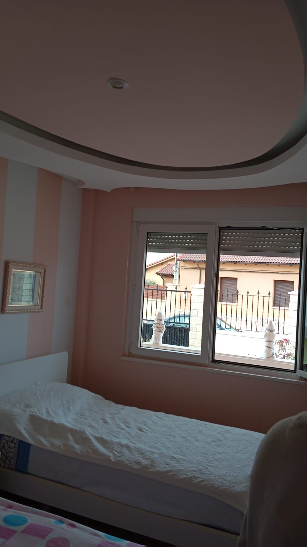 Dormitorio pequeño con una cama individual, paredes a rayas rosas y una ventana por la que entra la luz del día.
