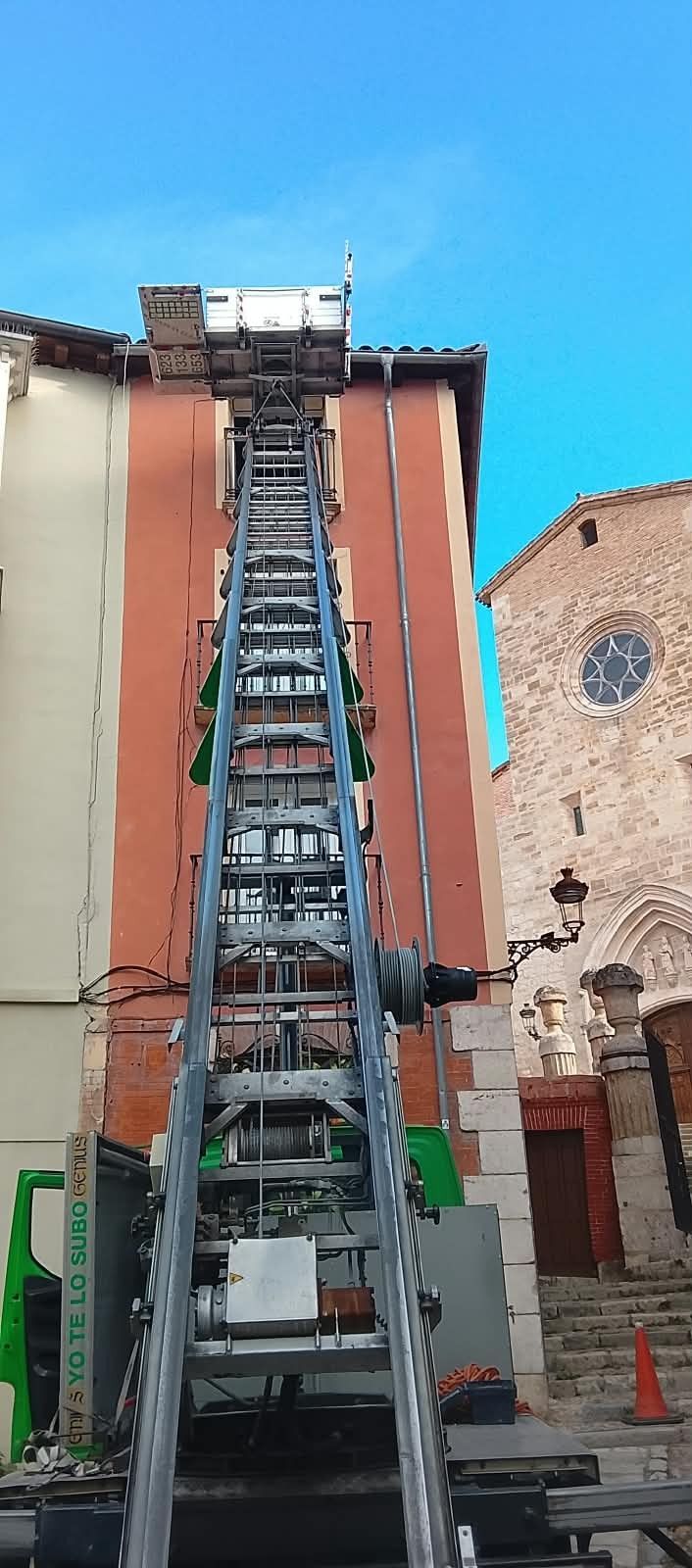 Elevador industrial alto o grúa frente a un edificio de ladrillo bajo un cielo azul despejado