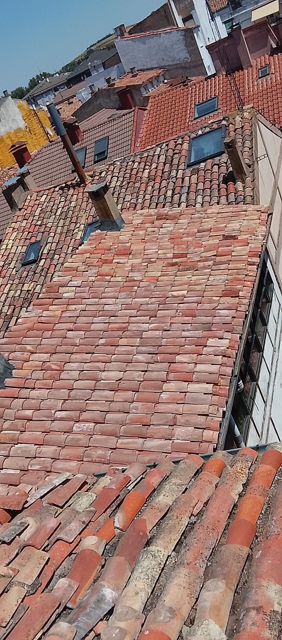 Un tejado de tejas rojas dañado, con partes rotas y madera expuesta en la pronunciada línea del tejado de un edificio.