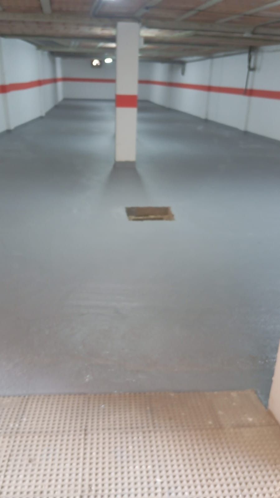 Garaje subterráneo vacío con columnas blancas y un suelo gris liso.
