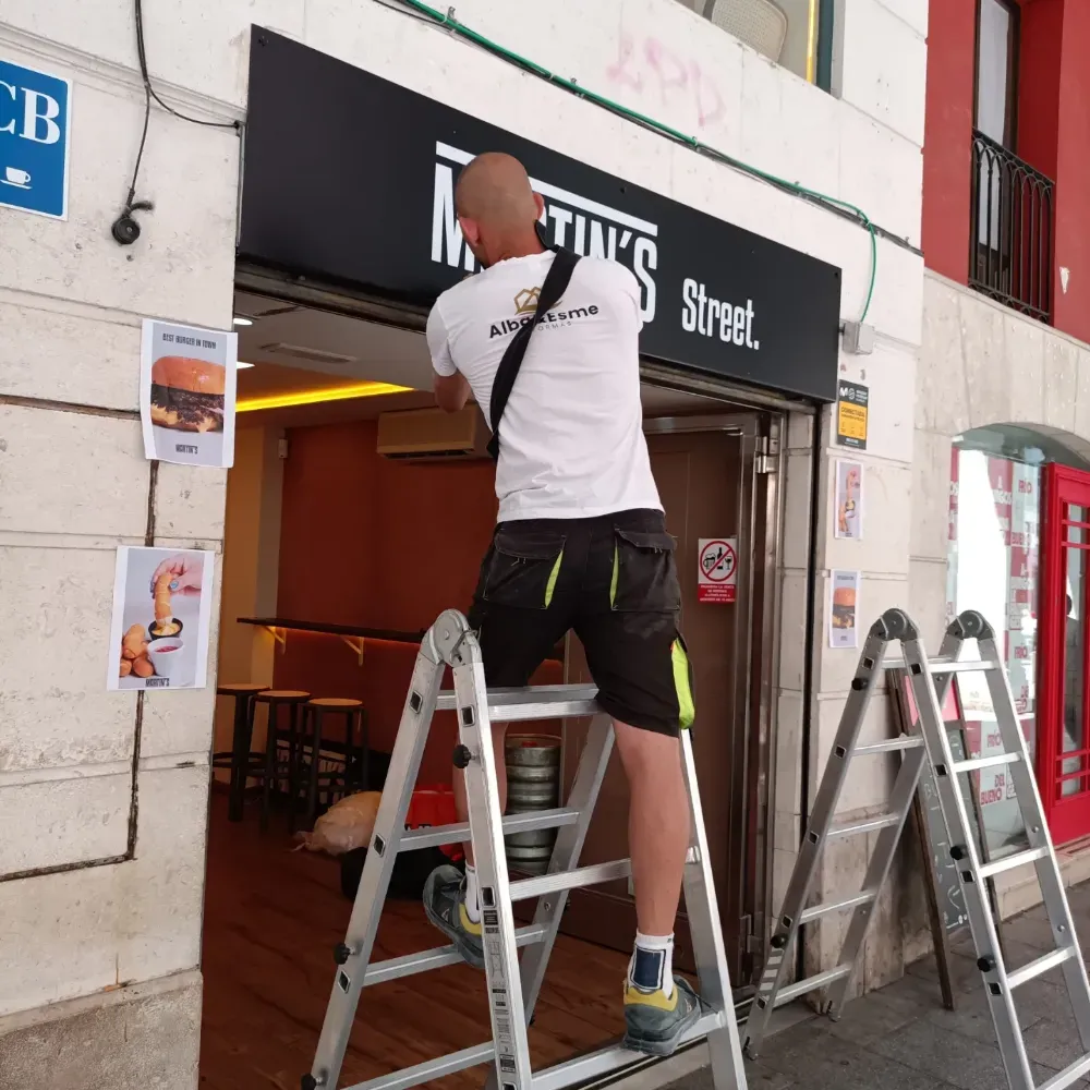 Un trabajador subido a una escalera arregla un letrero en la fachada de un pub.