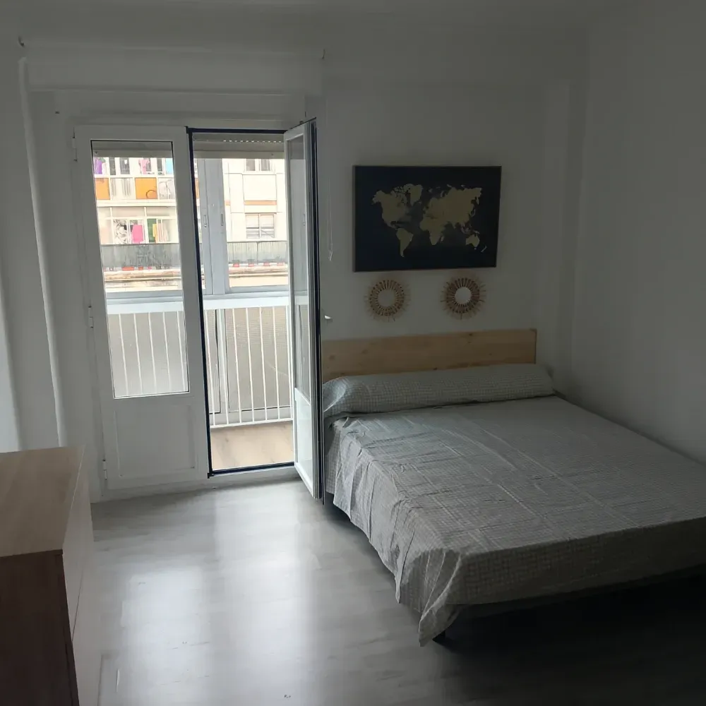 Habitación minimalista con cama, cuadros en la pared y puerta abierta a un balcón.