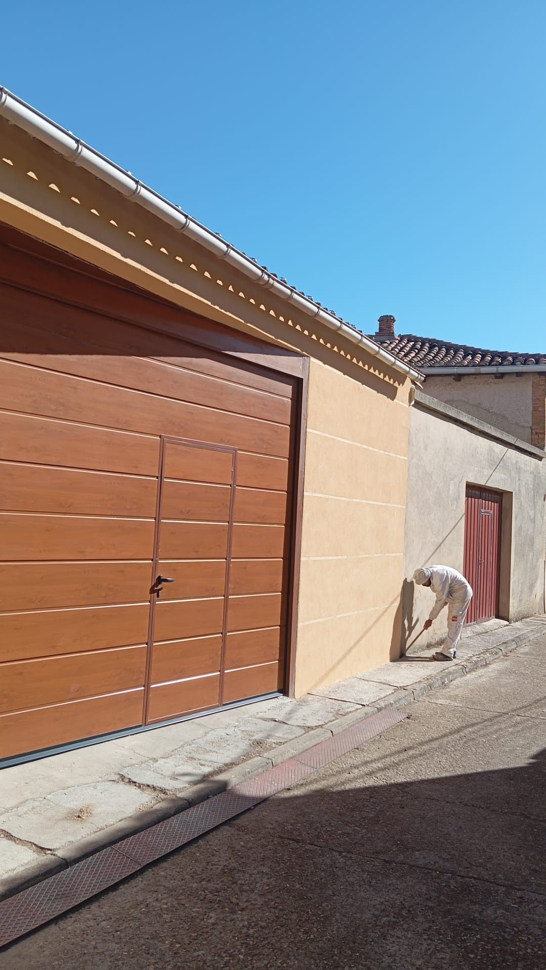 Callejón estrecho con una puerta de garaje marrón, paredes beige y un cielo azul intenso encima