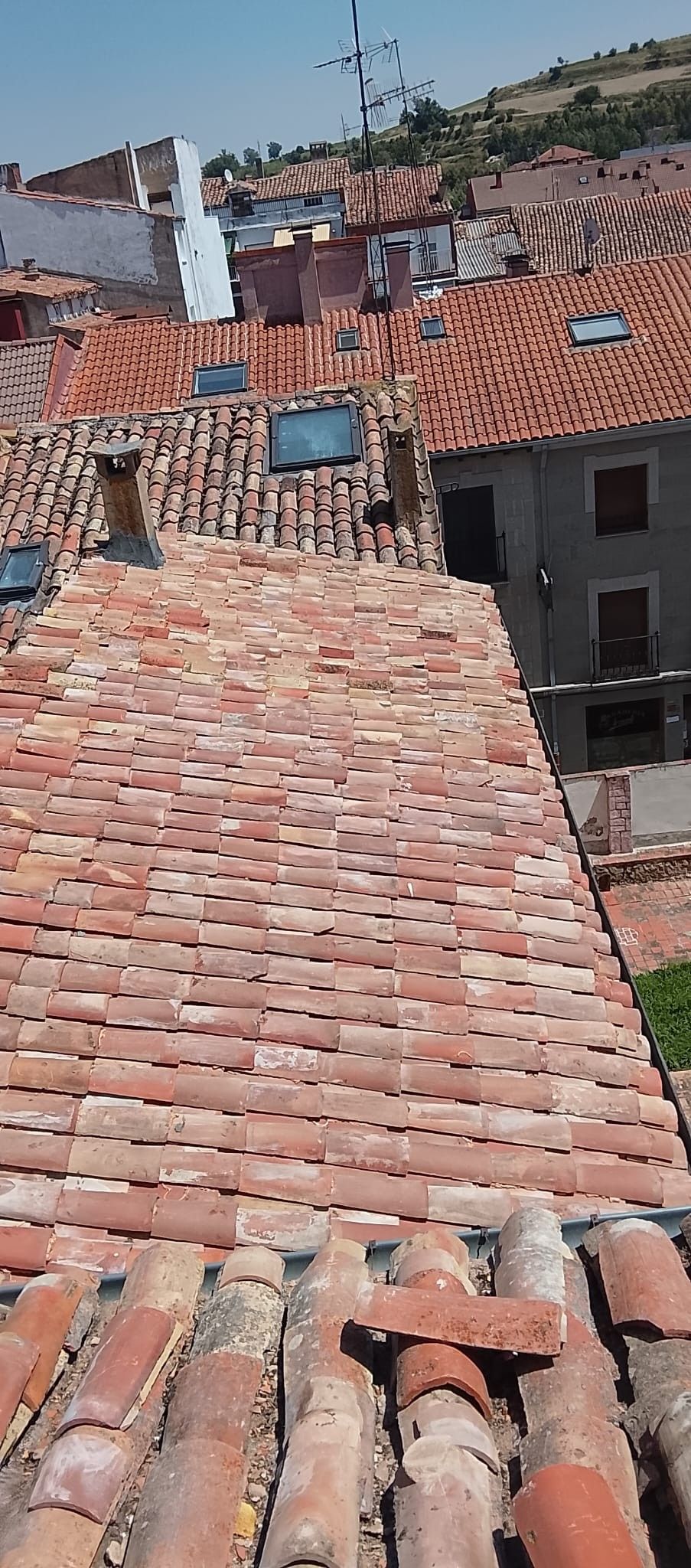 Tejados de tejas rojas en un pueblo de ladera, con chimeneas y un estrecho pasadizo entre tejados