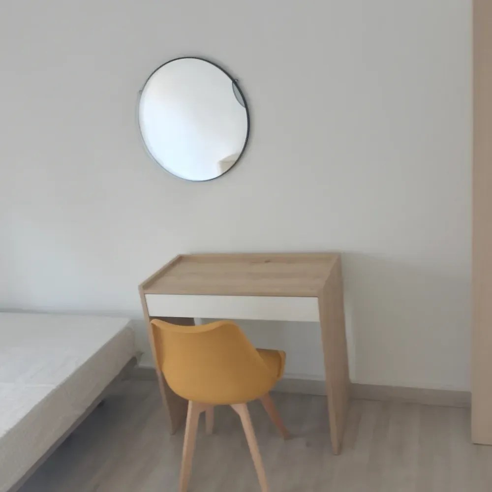 Escritorio pequeño de madera con silla amarilla en una habitación minimalista, con un espejo redondo encima.