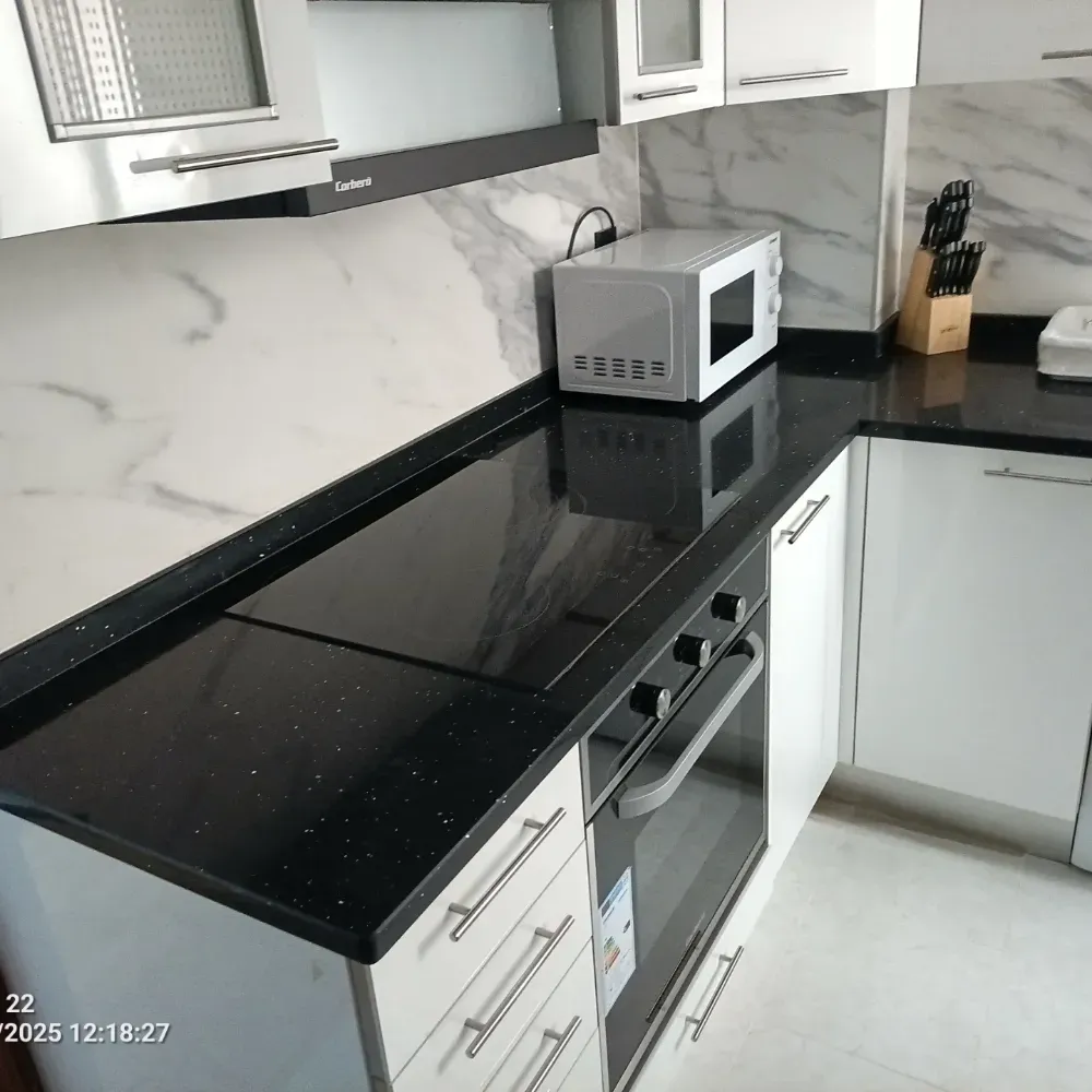 Cocina moderna con encimera negra, armarios blancos, microondas, vitrocerámica y soporte para cuchillos.