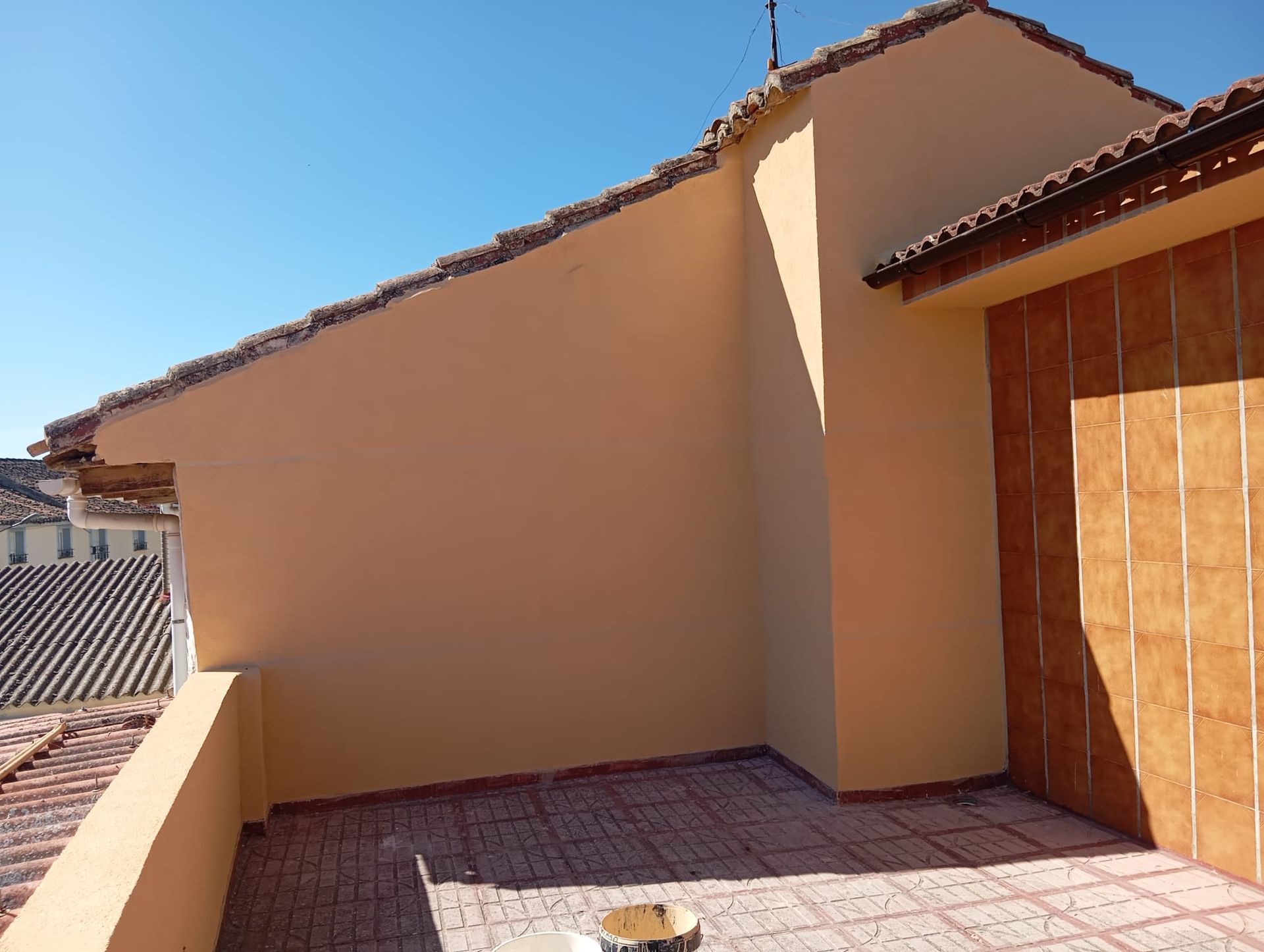 Terraza soleada en la azotea, con paredes color melocotón, suelo de baldosas y contraventanas de madera