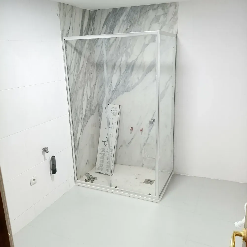 Cabina de ducha vacía con azulejos, paneles de pared con estampado de mármol y marco de vidrio en un baño en construcción.