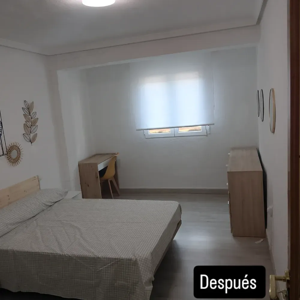 Habitación luminosa y minimalista con cama, escritorio, cómoda y una pequeña ventana con persiana.
