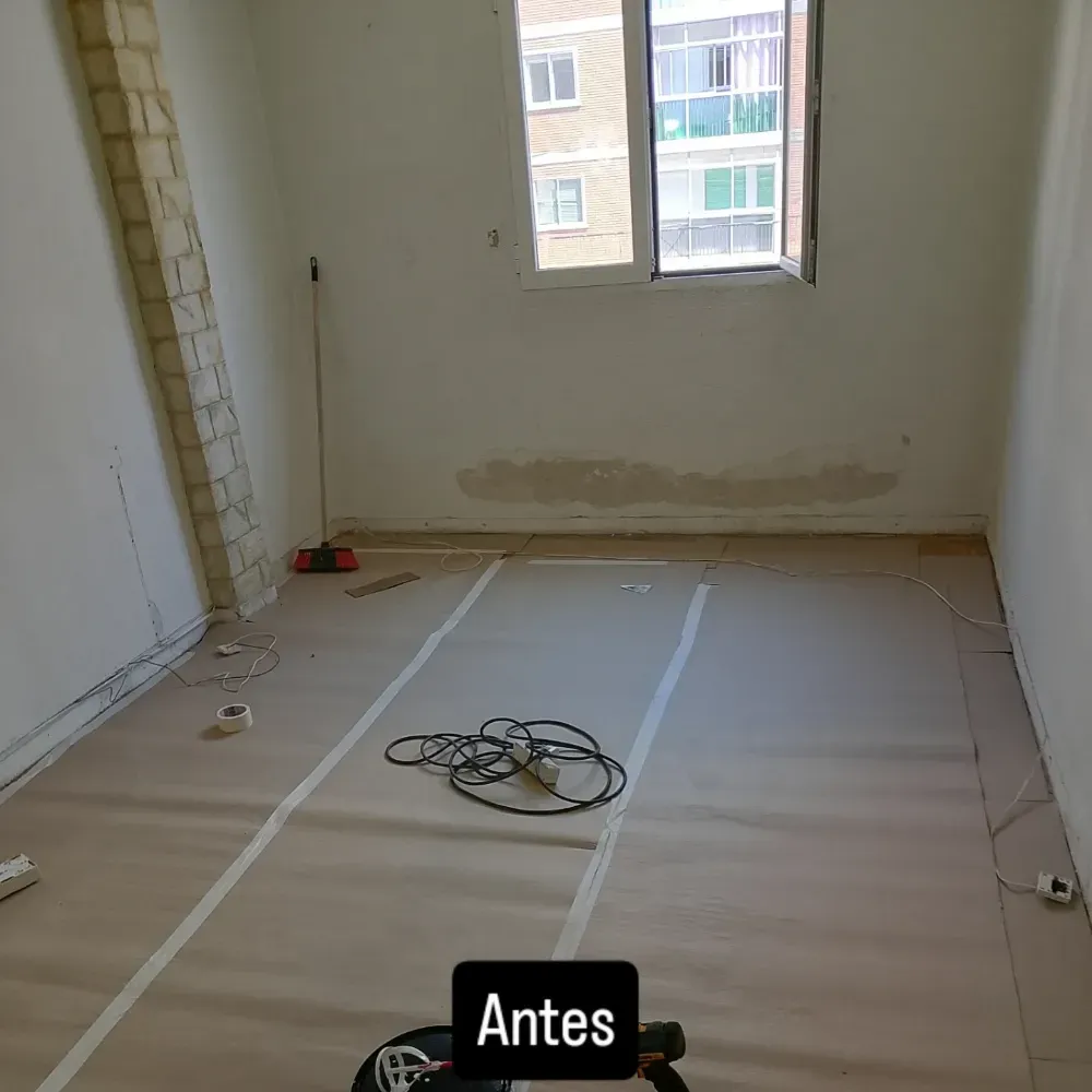 Habitación vacía en obras con suelo encintado, cable enrollado y luz de ventana; etiqueta “Antes” visible