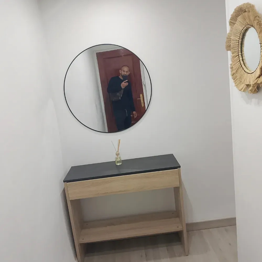 Consola minimalista para el recibidor con espejo redondo y decoración de pared tejida; persona reflejada en el espejo.