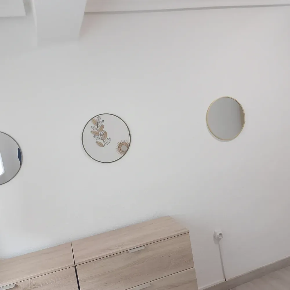 Pared blanca con tres espejos redondos sobre una cómoda de madera clara en una habitación minimalista.