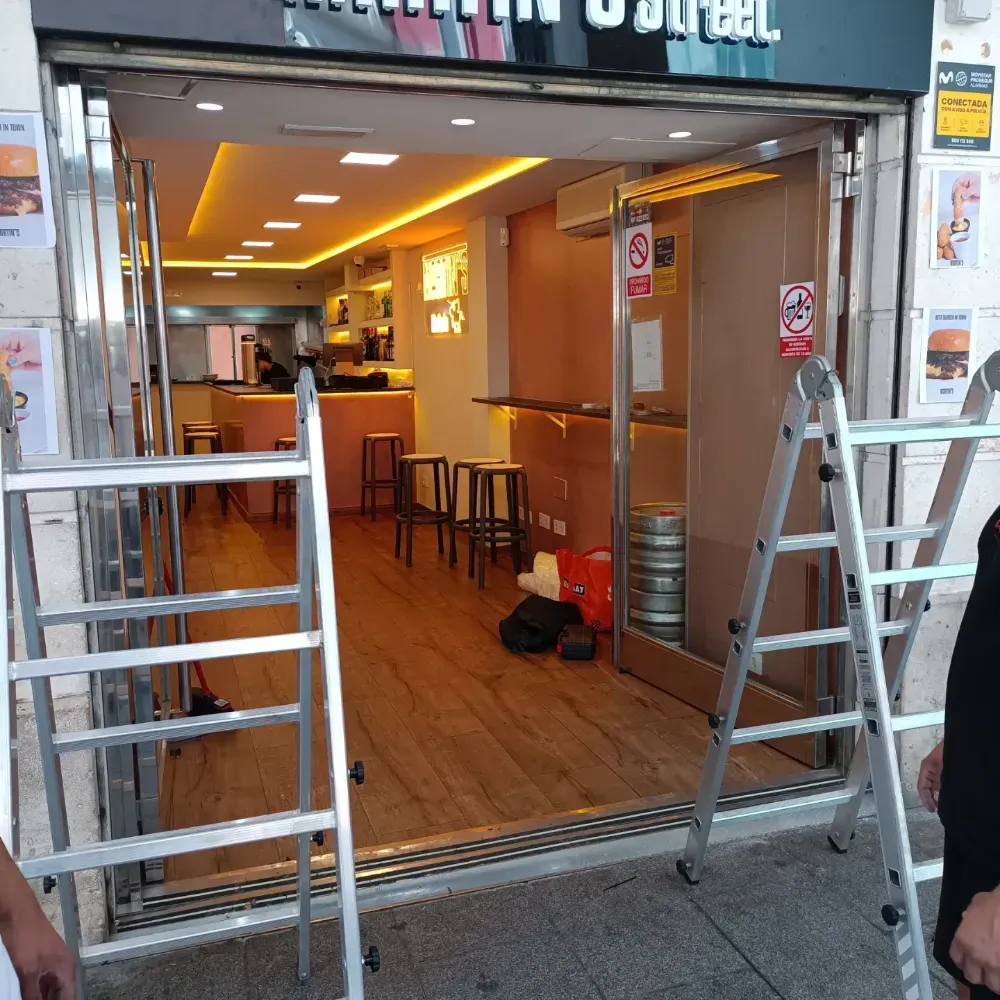 Local comercial abierto con suelo de madera, taburetes y escaleras en la entrada, visto desde la calle.