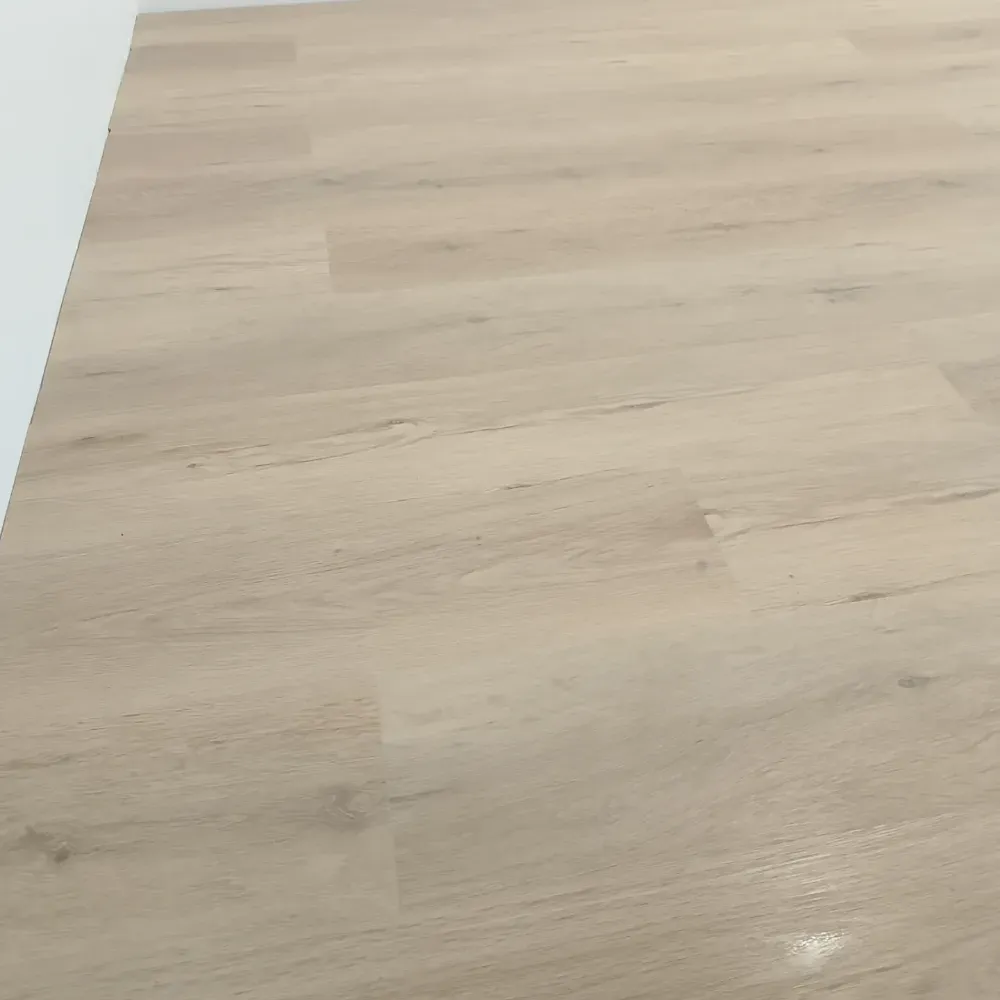 Suelo de madera clara con vetas sutiles y un pequeño reflejo brillante cerca de la parte inferior derecha.